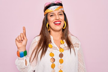 Sticker - Young hispanic hippie woman wearing fashion boho style and sunglasses over pink background pointing finger up with successful idea. Exited and happy. Number one.