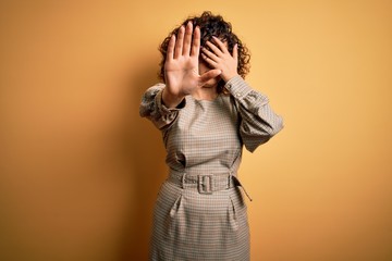 Sticker - Beautiful arab business woman wearing dress and glasses standing over yellow background covering eyes with hands and doing stop gesture with sad and fear expression. Embarrassed and negative concept.