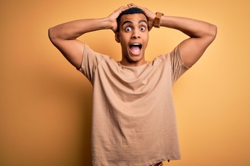 Wall Mural - Young handsome african american man wearing casual t-shirt standing over yellow background Crazy and scared with hands on head, afraid and surprised of shock with open mouth