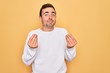© Krakenimages.com - Young handsome man with blue eyes wearing casual sweater standing over yellow background doing money gesture with hands, asking for salary payment, millionaire business