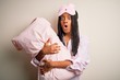 © Krakenimages.com - Young african american woman wearing pajama and eye mask hugging bed pillow scared in shock with a surprise face, afraid and excited with fear expression