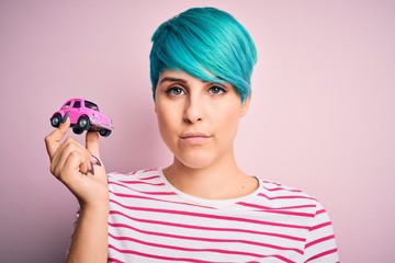 Sticker - Young business woman with blue fashion hair holding small car as rental and insurance with a confident expression on smart face thinking serious