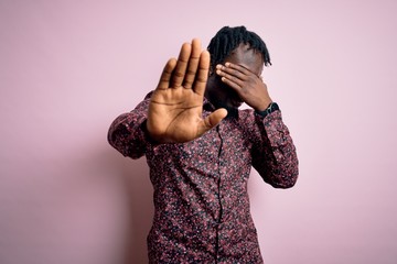 Canvas Print - Young handsome african american man wearing casual shirt standing over pink background covering eyes with hands and doing stop gesture with sad and fear expression. Embarrassed and negative concept.