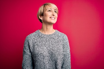 Sticker - Young blonde woman with modern short hair wearing casual sweater over pink background looking away to side with smile on face, natural expression. Laughing confident.