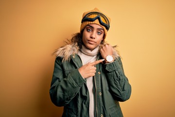 Poster - Young african american afro skier girl wearing snow sportswear and ski goggles In hurry pointing to watch time, impatience, looking at the camera with relaxed expression