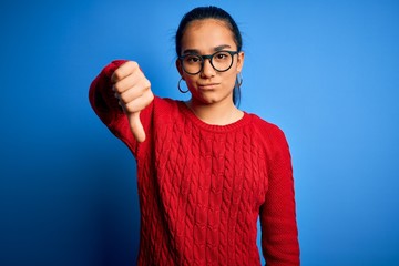 Canvas Print - Young beautiful asian woman wearing casual sweater and glasses over blue background looking unhappy and angry showing rejection and negative with thumbs down gesture. Bad expression.