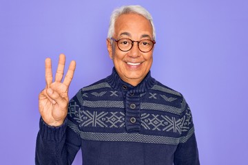 Middle age senior grey-haired man wearing glasses and winter sweater over purple background showing and pointing up with fingers number three while smiling confident and happy.