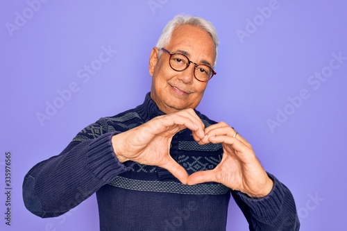 Cuadros en Lienzo Middle age senior grey-haired man wearing glasses and winter sweater over purple background smiling in love doing heart symbol shape with hands