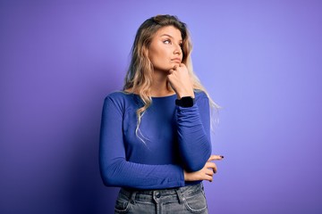 Poster - Young beautiful blonde woman wearing casual t-shirt over isolated purple background with hand on chin thinking about question, pensive expression. Smiling with thoughtful face. Doubt concept.