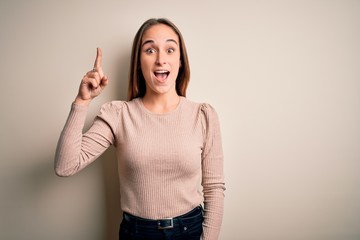 Young beautiful woman wearing casual sweater standing over isolated white background pointing finger up with successful idea. Exited and happy. Number one.