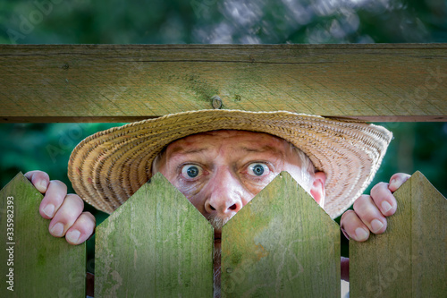 Fotomural An elderly man in a straw hat looks curiously over a garden fence