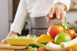 © DragonImages - Close-up image of cook taking fresh ripe tomato from bowl to cut it for salad