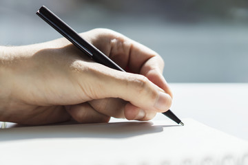 man writes with a pen in notepad in a sunny office, business and education concept. close up