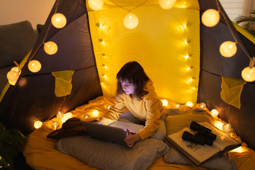 Wall Mural - little 11 year old girl using laptop under her home-made tent inside the living room.