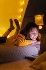 Wall Mural - little 11 year old girl using laptop under her home-made tent inside the living room.