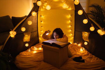 Wall Mural - young female child reading encyclopedia in a home made livingroom tent with light balls.