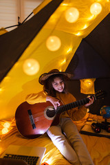 Wall Mural - little girl playing acoustic guitar under the tent in a living room.
