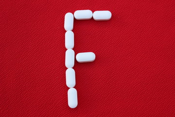 Alphabet made of pills on a red background. Abc from drugs. 
Letter F made from pills. Capital letter F of medicines