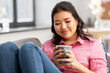 © Syda Productions - people and leisure concept - happy smiling asian young woman in pink shirt sitting on sofa and drinking coffee at home