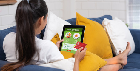 Poster - Asian woman order food online with credit card on tablet sitting on sofa at home.digital lifestyle with technology