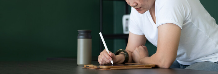 Poster - asian woman writing on tablet on table at home.work from home while coronavirus outbreak.leave space for add text.banner mockup
