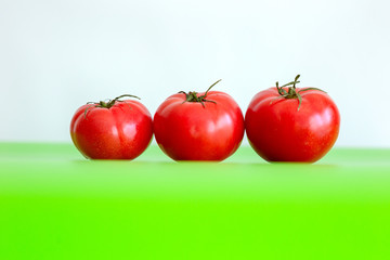 Three large red juicy fresh tomatoes lie on a green table. Close-up. White background.