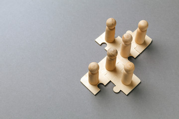 Wooden figures on puzzles on grey background as a symbol of team building. Organization group people in business. Cooperation and partnership.