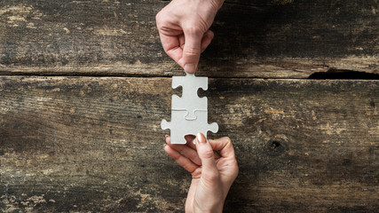 Wall Mural - Male and female hands joining two matching puzzle pieces