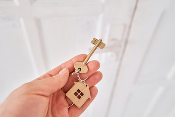 Modern light lobby interior. Men hand holding key with house keychain. Real estate, moving home or renting property. Mortgage concept.