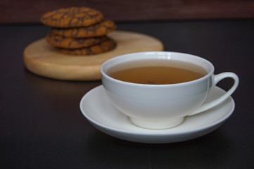 Tea party. Tea in a white mug with homemade oatmeal cookies with chocolate icing on top. Dark background.