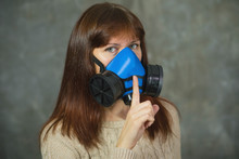 Young Woman In Respirator Shows Sign Of Silence On Grey Background. Virus Protection Concept.
