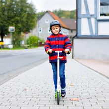 Cute Little School Kid Boy With Helmet Riding On Scooter In Park Nature. Children Activities Outdoor In Winter, Spring Or Autumn. Funny Happy Child In Colorful Fashion Clothes.