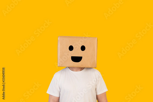 Fotomural Hombre con caja de cartón en la cabeza con una sonrisa en la cara sobre fondo amarillo liso brillante