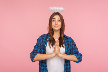 portrait of angelic kind pretty girl with nimbus over head holding hands in prayer gesture and looki