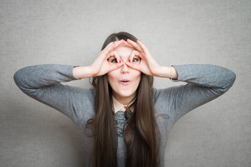 Wall Mural - Young happy woman holding her hands over her eyes as glasses and  looking through fingers