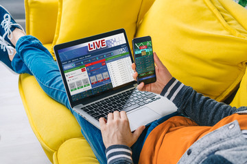 Cropped shot of a man lying on sofa making bets online at bookmaker's website using laptop