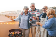 Happy Senior Friends Having Fun Cheering With Red Wine At Barbecue On Terrace - Mature People Dining And Laughing Together At Bbq Party - Food Drink And Elderly Friendship Lifestyle Concept