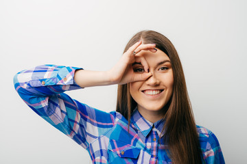 Wall Mural - Young happy woman holding her hand over her eye as glasses and  looking through fingers