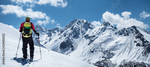Plakaty Sporty Zimowe  widok-z-tylu-aktywnego-czlowieka-na-nartach-turystycznych-na-tle-gor-w-sloneczny-zimowy-dzien