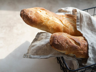 Two crisp fresh homemade french baguettes in a black metal basket in the sun on table