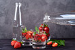 Detox infused water pouring from bottle into glass with strawberry and mint on dark wood table background, copy space. Cold summer drink. Mineral water