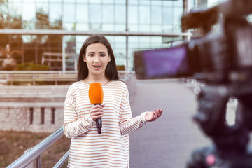 Canvas Print - Young female journalist with microphone working on city street