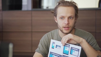 Wall Mural - young man having business video call on cell phone placed on tripod and showing printed web interfac