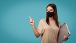 © South House Studio - Brunette woman in medical mask holds laptop computer and pointing to copy space