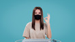 © South House Studio - Cute brunette female in mask shows ok sign isolated over blue bg