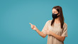 © South House Studio - Brunette cute woman in mask pointing her fingers to copy space isolated over blue background
