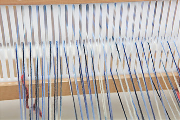 Wood and plastic weaving heddle with blue and white wool warped around it, weaving loom vintage industry tool to manufacture textile by hand Close-up on yarn