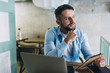 © BullRun - Creative male entrepreneur working on freelance in coffee shop pondering on ideas for business using laptop computer, contemplative hipster guy with planner concentrated on freelance research