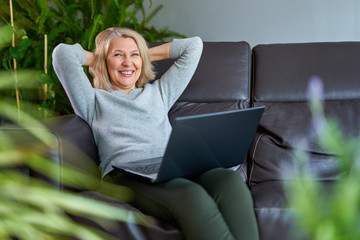 Wall Mural - Happy woman on a sofa at home concentrating as she works on a laptop.