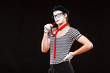 Portrait of male mime artist performing, isolated on black background. Man in beret and striped T-shirt put his red tie in his mouth